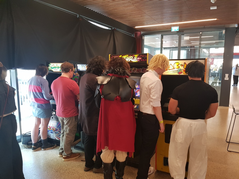 Some people playing arcade games at Q-Con. The games are, from left to right: Galaga, Bubble Bobble, Street Fighter II Champion Edition, and Pac-Man.
