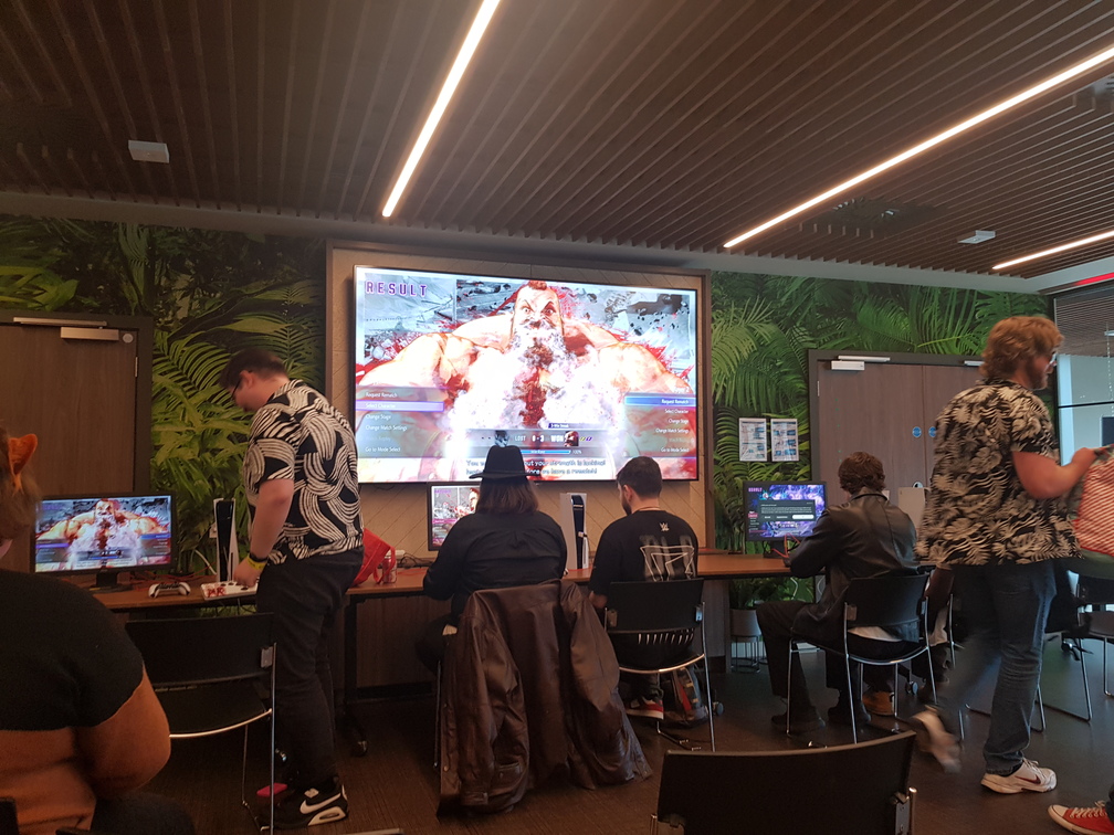 General view of the fighting game tournament area during the SF6 tournament. There are four setups, and the leftmost one is mirrored on the main screen.